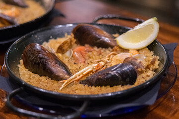 Fototapeta premium Seafood paella with mussels, shrimp, clams, and crayfish, served in a traditional paella pan and garnished with a slice of lemon.