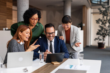 Diverse Business Team Smiling During Collaborative Office Meeting Around a Laptop