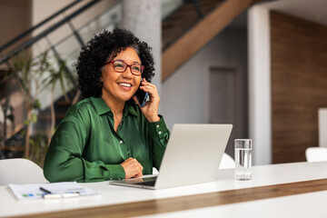 Professional Woman Working Remotely Using Laptop and Phone in Modern Office