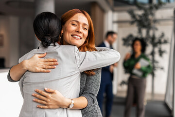 Two Women Cheerfully Hugging in a Business Environment