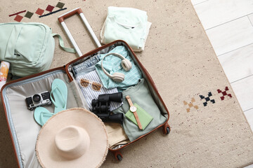 Unpacked suitcase with clothes, hat and accessories at home, top view