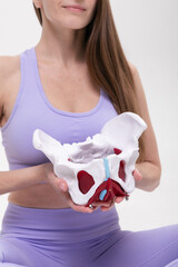 Woman in Lavender Fitness Wear Holding Anatomical Pelvis Model on White Background