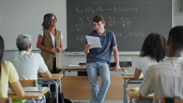Young teenager student reading essay presentation to classmates and teacher at High School