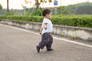 Fototapeta premium The baby is walking on the sidewalk, holding a toothbrush in his hand. The scene takes place near some bushes and trees, giving it a more natural setting.