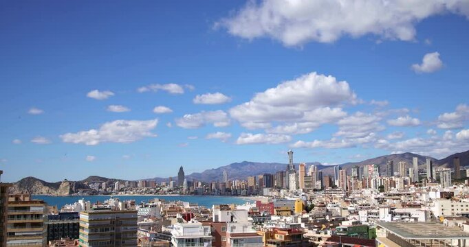Time lapse footage over looking the Spanish old town of Benidorm in Spain showing clouds in the blue sky passing by over two hours on the timelapse aerial video on a sunny summers day