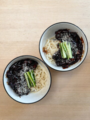 Two bowls of black bean noodles with cucumber.