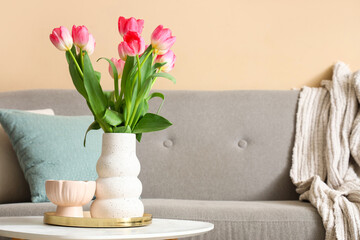 Vase with tulips and candle on table in living room decorated for Women's Day, closeup