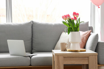 Vase with tulips and cup of tea on table in living room decorated for Women's Day