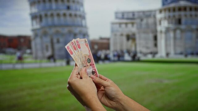 Man holding uae dirham in pisa with the leaning tower in the background showcasing cultural exchange and travel finance.