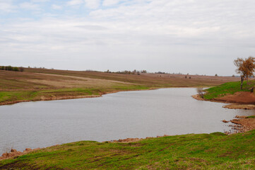 Country landscape in spring time, small river with gentle banks, farm fields on the other side of the river, cloudy sky