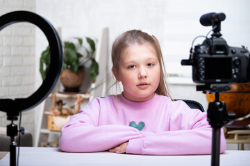 A beautiful blonde teenager is broadcasting live. The video blogger has a live broadcast. An annular lamp and a camera during a live broadcast of a video blogger