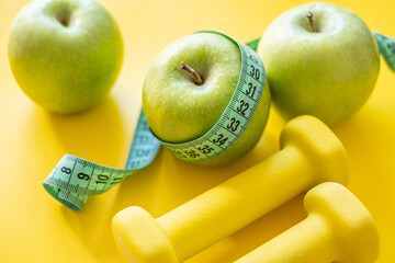 Green apples with measuring tape and dumbbells on yellow background