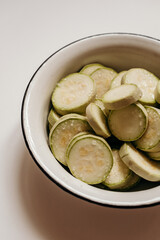 A white bowl filled with sliced ​​fresh zucchini slices on a white background. Perfect for cooking recipes, healthy eating or minimalist style
