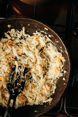 Shredded cabbage and onions are fried in a pan, the shoulder blade is on top. The aromatic dish on the stove creates the atmosphere of home cooking and a warm lunch.
