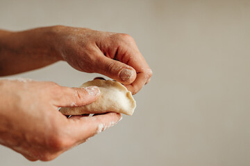 Female hands are molding dumplings on a kitchen table sprinkled with flour. Round dough blanks are cut out nearby. Home cooking, preparation of traditional dishes
