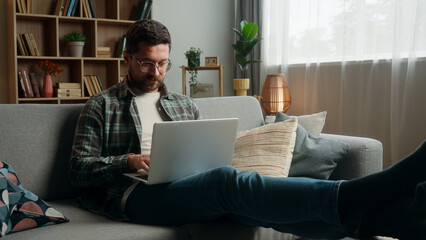 Happy smiling positive Caucasian man male guy at home couch sofa with laptop computer working...