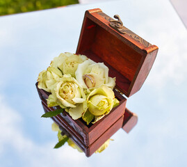 Close-Up of Wedding Rings on White Roses in Wooden Box