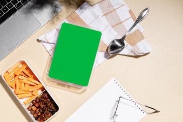 Healthy snack at the workplace in the office mockup.  Carrot sticks and a mix of nuts and dried fruits are arranged in a rectangular lunchbox on a checked cloth. 