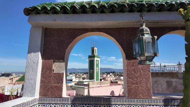 Traditional moroccan window framing the minaret of the Grand Mosque of Meknes, with a colorful lantern, under a blue sky
