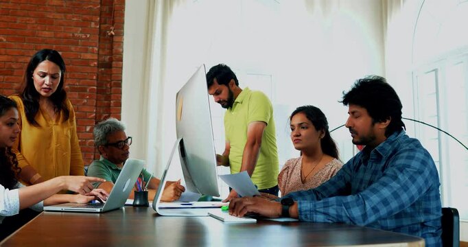 Indian Asian young business professionals or technology startup partners working on computer, suddenly celebrating success with high-fives cheers, sitting at desk with a laptop in modern cozy office