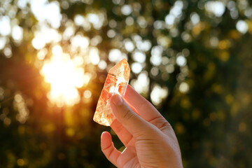 quartz crystal in hand outdoor, abstract natural sunny background. Esoteric spiritual practice with...