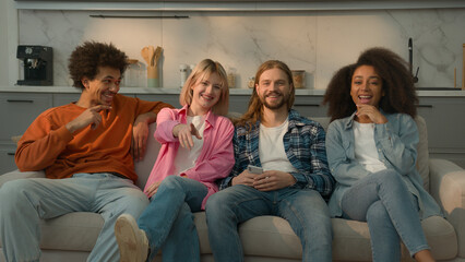 Multiracial group of friends multiethnic diversity people men Caucasian guys buddies African American girl women relaxing together at home couch sofa watching TV funny laugh fun laughing television