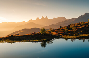 Golden sunrise over Arves massif with lonely tree relfection on Lac Guichard at French Alps