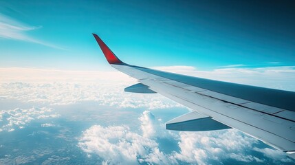 Obraz premium A clean shot of an airplane wing against a backdrop of a vivid blue sky, with a few clouds drifting below.