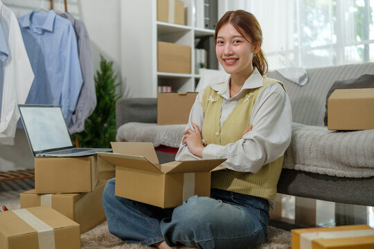 Smiling young entrepreneur sitting among packed boxes, preparing shipments for her online store. E-commerce and online business concept.