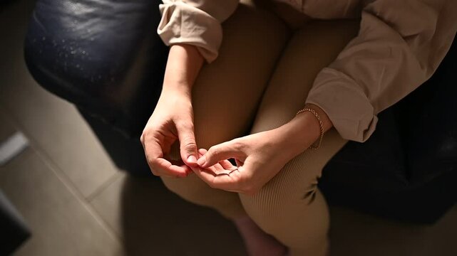 The woman nervously twists her fingers and picks at her fingers