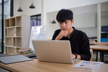 Thoughtful young businessman working on a laptop, analyzing data.