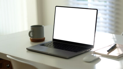 Contemporary work desk with a laptop, coffee mug, and stationery bathed in natural light from the window.