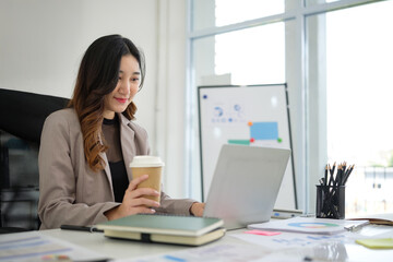 Successful businesswoman is focused on her work, sipping coffee as she types on her laptop.