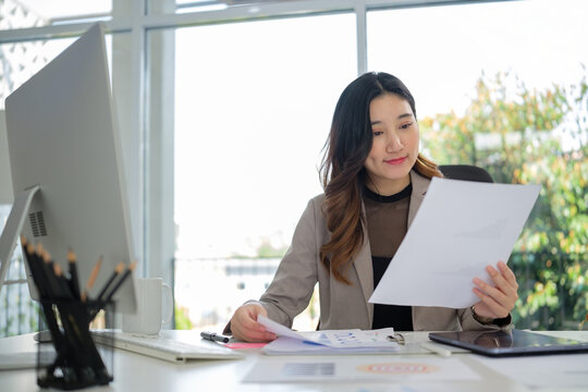 Young executive examines a report while working on financial planning at her organized office desk.