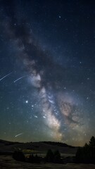 Cosmic display of the Milky Way with shooting stars in a clear night sky over a remote landscape vertical
