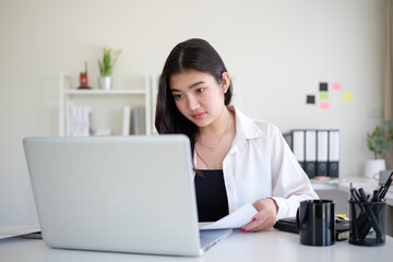 Confident woman manages her work tasks, reviewing documents and data in a bright, modern office setup.