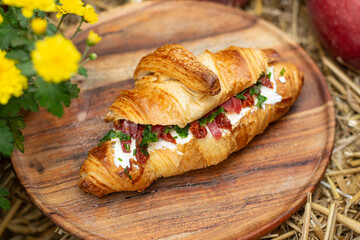 Croissant with bacon, herbs, cream cheese and sun-dried tomatoes on a wooden plate, autumn rustic serving with apples and flowers