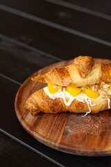 Delicious croissant with cream cheese, canned peach slices and walnuts on a wooden plate, autumn picnic dessert concept, closeup