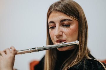 Portrait of a young woman performing on a flute in an indoor setting. The focused expression and precise finger placement convey a deep dedication to music. Ideal for concepts of art and talent.