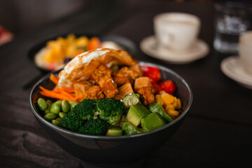 Salad bowl mix with edamame, broccoli, tofu and fried egg. Delicious lunch with vegetables on a wooden table