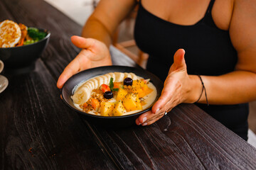 Woman is holding porridge with pieces of mango, nut granola, bananas and berries. Delicious oatmeal with fruit for breakfast
