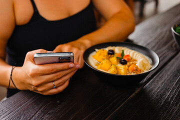 A woman has breakfast of porridge with fruits, berries and holds a phone in her hands. The concept...