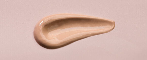 Makeup foundation, BB cream smear, cosmetic product over beige background. Make up base skin care, foundation, concealer smudge close up. Skin corrector, beauty facial treatment stroke. Top view. 