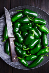 Green mexican jalapeno hot peppers on black plate with knife close up. Food photography