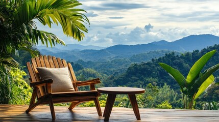 Obraz premium A wooden chair with a pillow and a round table on a scenic terrace, with lush green mountains and blue skies in the background.