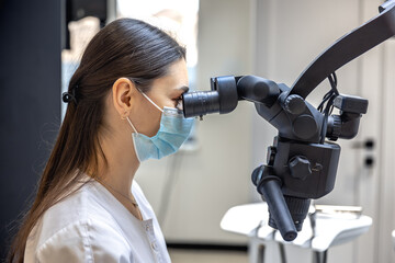Fototapeta premium Young female dentist treating patient's teeth with dental microscope. Dentistry concept.