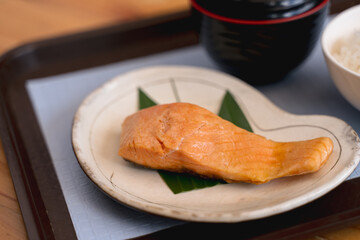 Japanese-style meal with grilled salmon, a bowl of rice, and an empty soup bowl on a tray.