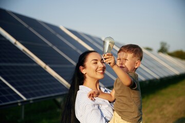 Taking a look at the light bulb. Mother with her little son are near the solar panels
