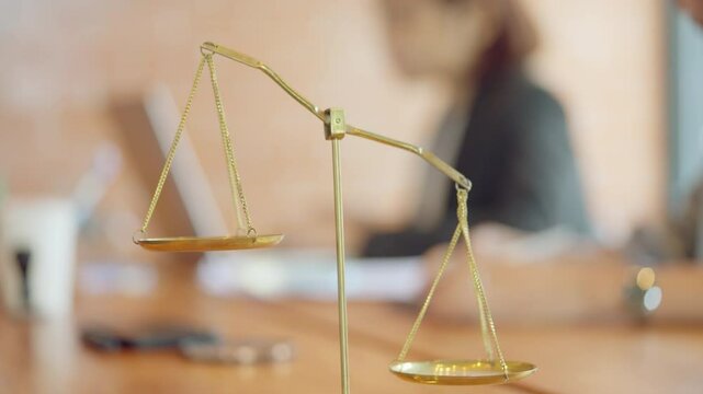 A scale with a woman in the background. The scale is gold and has a woman's head on it