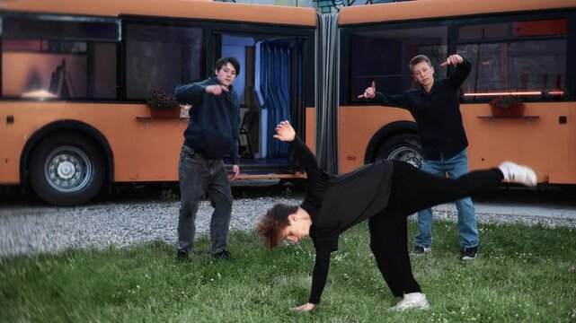 Breakdancing performers executing dynamic hip-hop moves on grassy ground, displaying street culture near bright orange bus